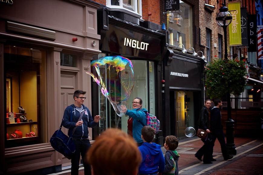 Woman making giant rainbow bubble for children on city street