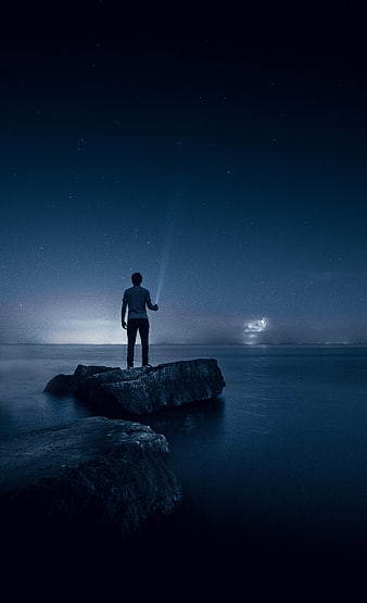 Man standing on rock at night with flashlight under starry sky
