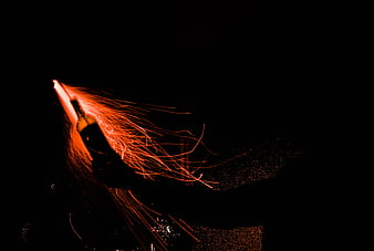 Hand holding glowing sparkler with flying sparks in the dark