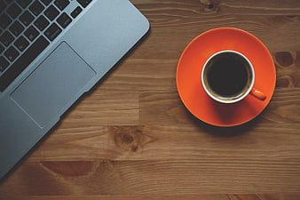 Laptop and orange coffee cup on wooden desk