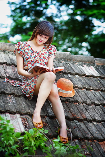 Young Woman Reading Book on Roof with Floral Dress