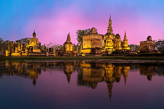 Ancient Temple Ruins with Golden Buddha Statue Reflected in Water at Sunset