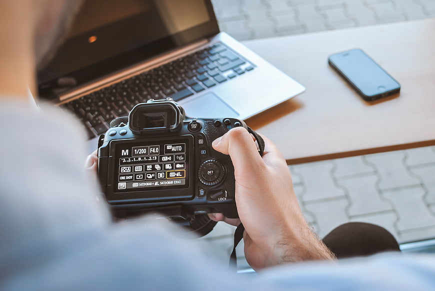 Photographer reviewing camera settings with laptop and smartphone