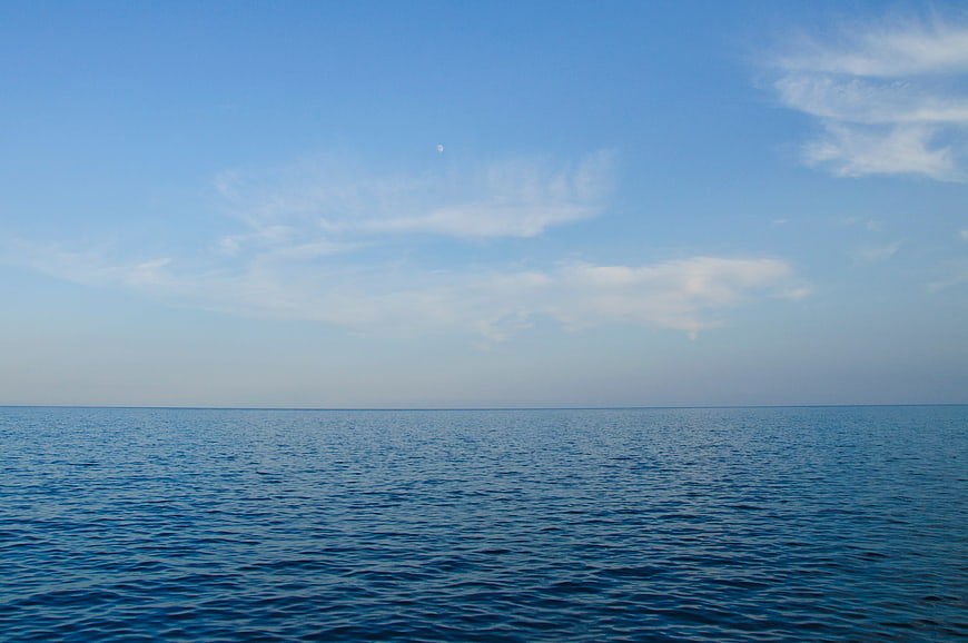 Serene Blue Ocean Horizon with Wispy Clouds and Moon