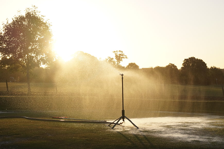 Sprinkler watering golf course grass at golden hour sunset