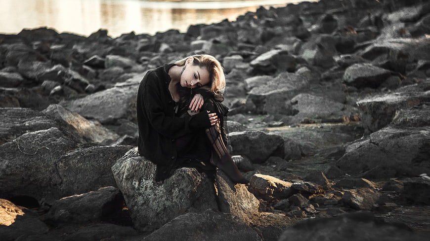 Melancholic Woman Sitting on Rocks by Water
