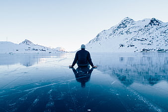Man meditating on frozen lake with snowy mountains
