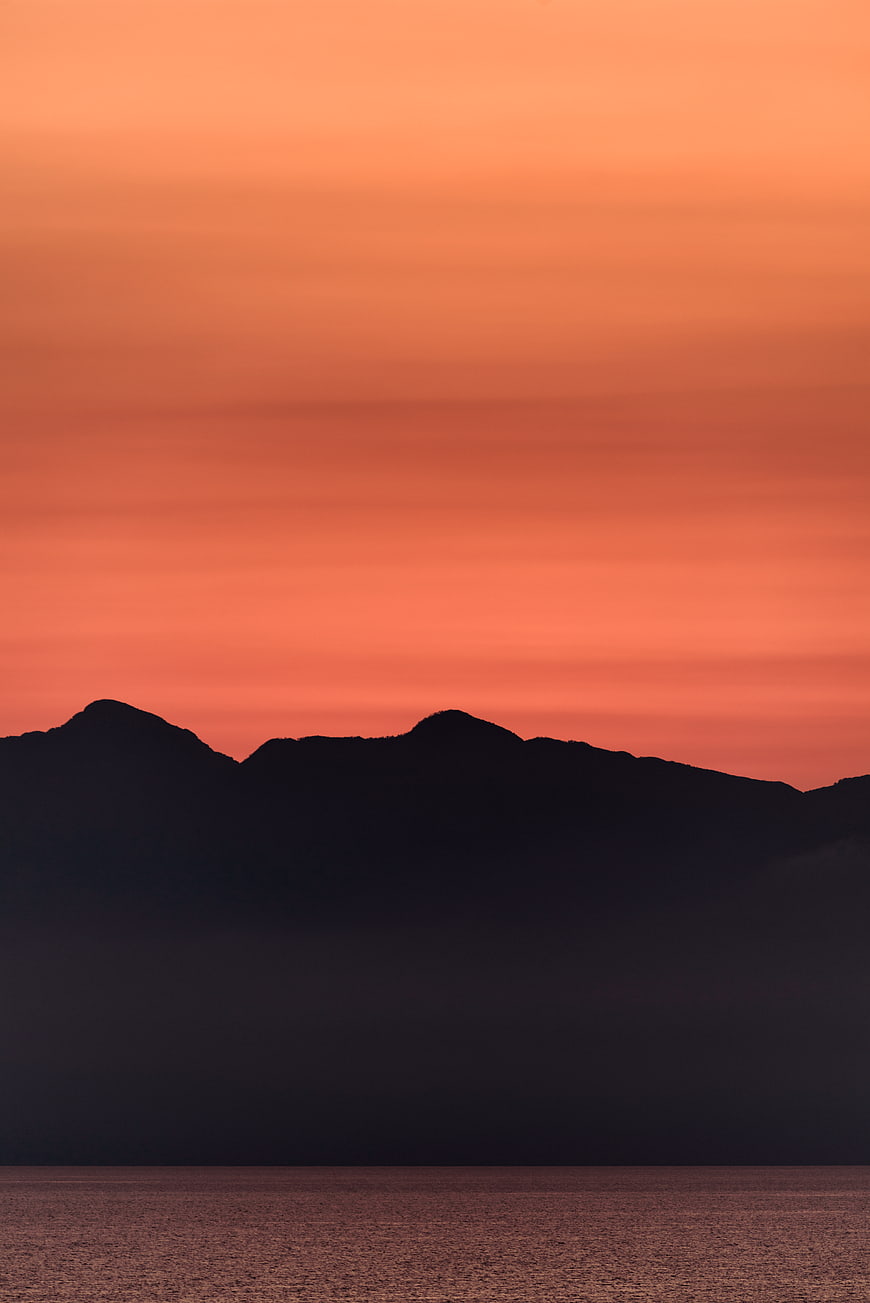 Silhouetted Mountain Range Against Vibrant Orange Sunset Sky