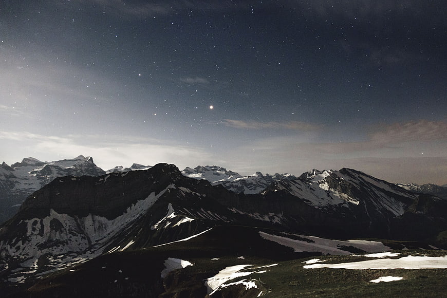 Snowy mountain range under starry night sky with moon