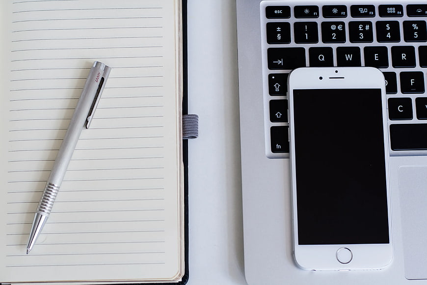 Flat lay of notebook, pen, laptop, and smartphone workspace