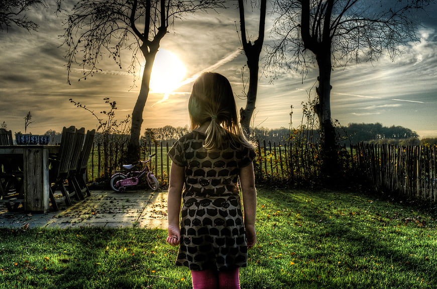 Little Girl Standing in Garden at Sunset with Bicycle