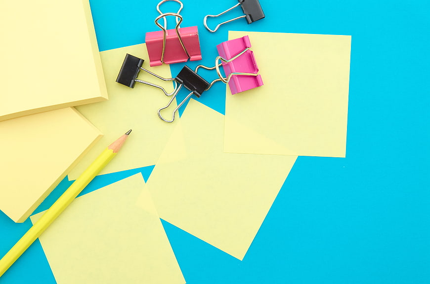 Flat lay of yellow sticky notes, binder clips, and pencil on blue background