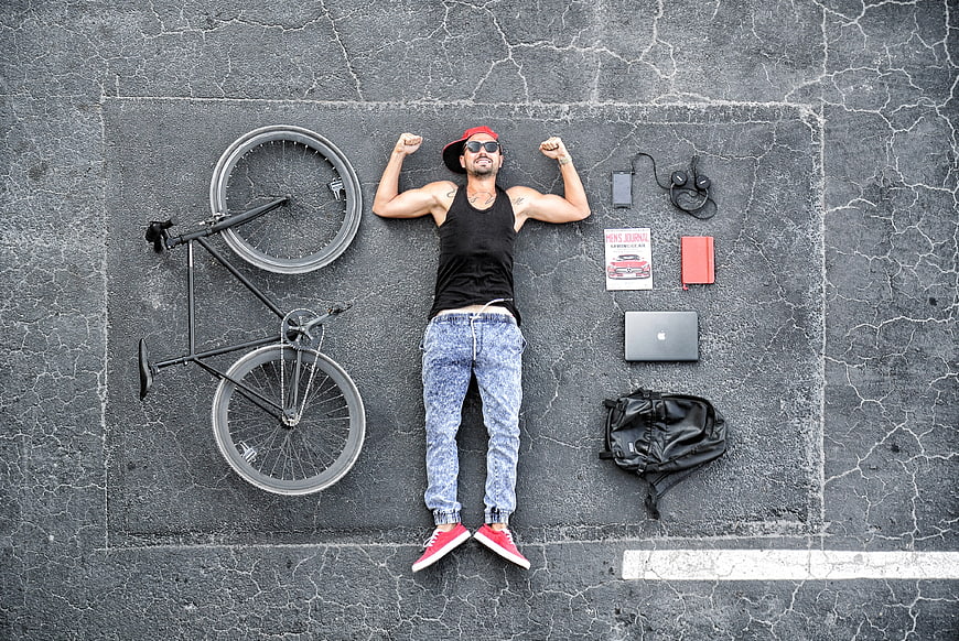 Top view of man lying on asphalt with bicycle and tech essentials