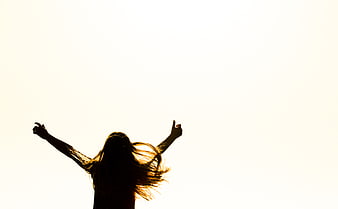 Silhouette of woman with arms raised in joy against bright sky