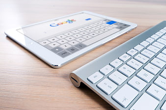 White tablet and silver keyboard on wooden desk