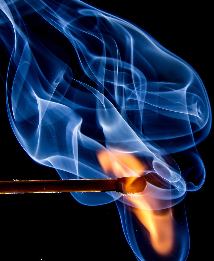 Burning matchstick with vibrant blue smoke against black background