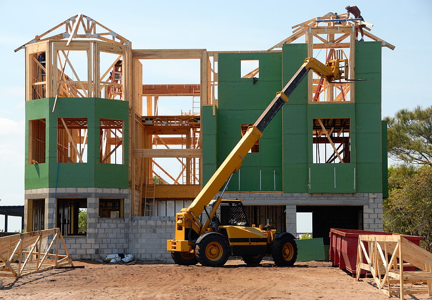 Construction site with yellow telehandler and unfinished house frame