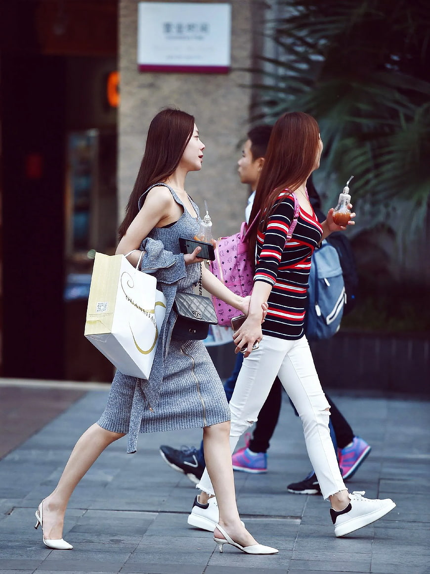 Two women walking with shopping bags and drinks on city street