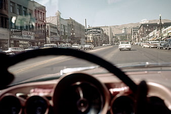 Vintage POV driving down a 1950s city street with classic cars