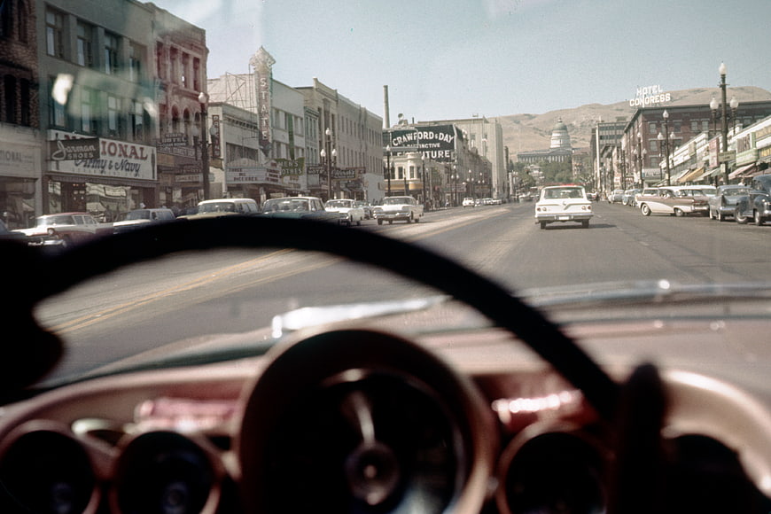 Vintage POV driving down a 1950s city street with classic cars