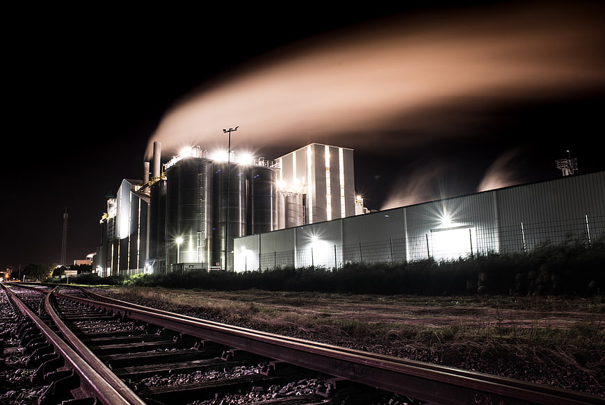 Industrial Factory at Night with Smoke Plume and Train Tracks