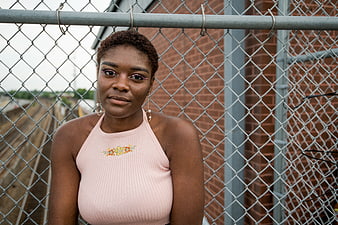 Portrait of young black woman in pink top by chain link fence