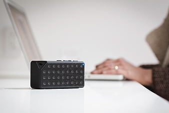 Black portable speaker on white desk with blurred laptop background