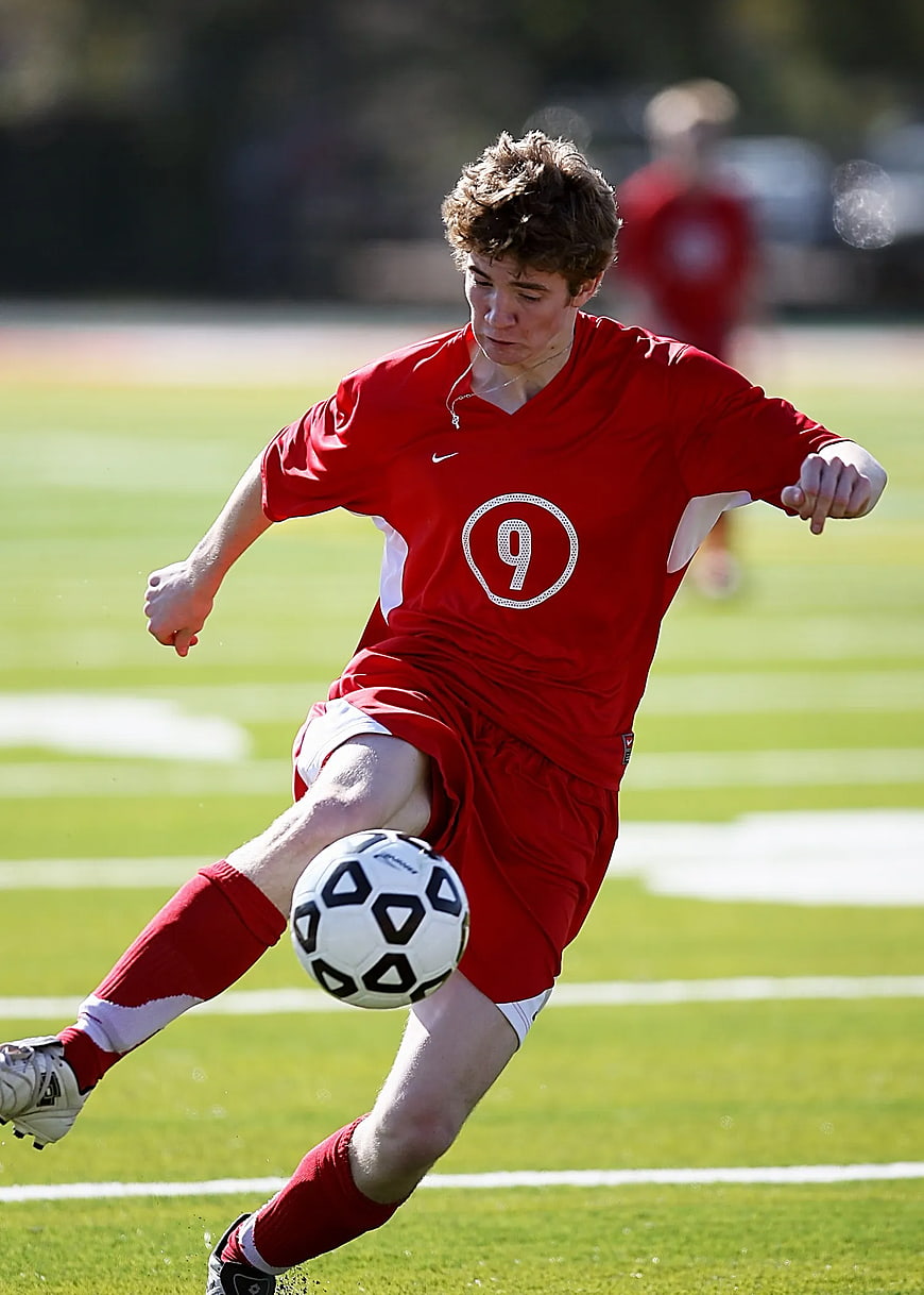 Young Soccer Player Kicking Ball on Green Field