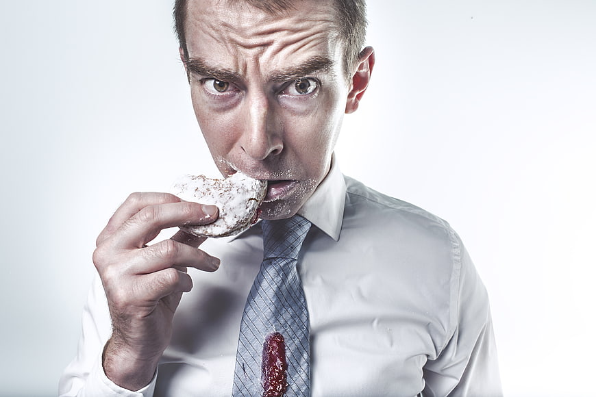 Messy businessman eating donut with powdered sugar and jam stain