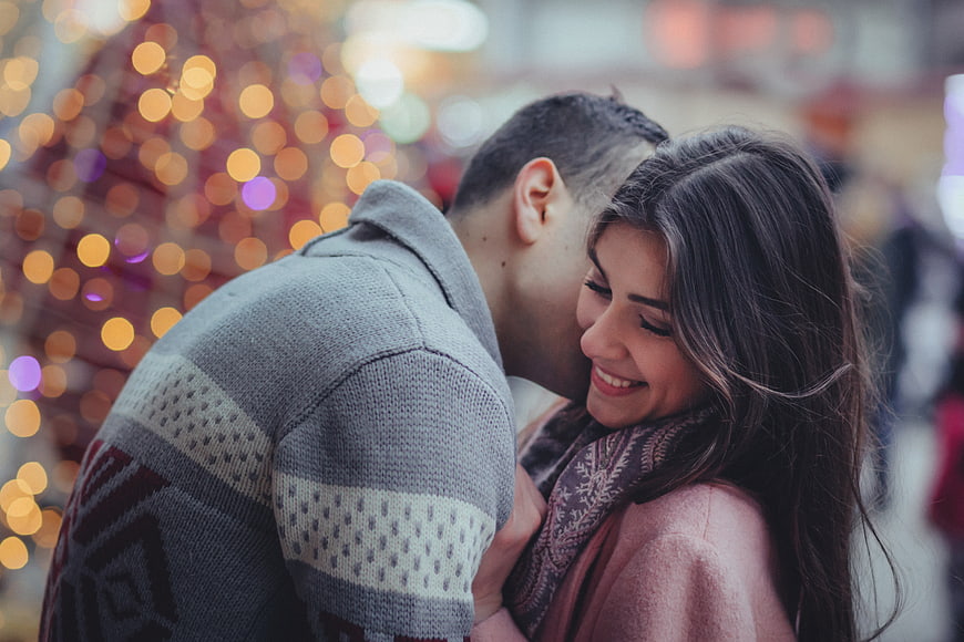 Romantic couple kissing with Christmas bokeh lights background