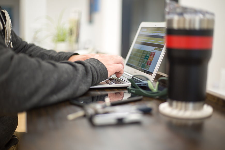 Freelancer typing on laptop at wooden desk with coffee