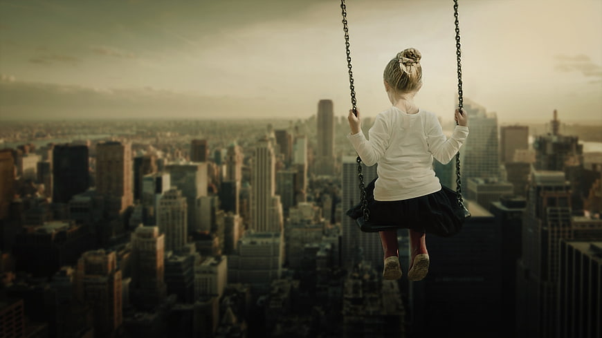 Little girl swinging high above a city skyline