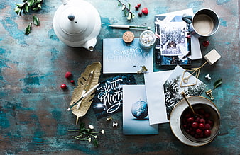 Flat lay of Christmas cards, teapot, and berries on blue table
