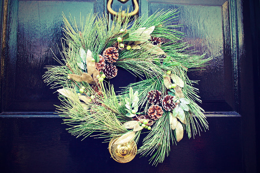 Christmas wreath with pine cones and gold bell on dark door