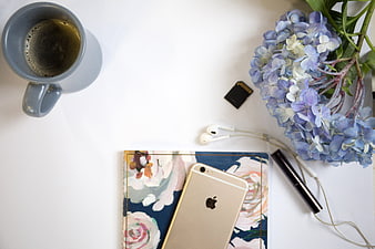 Flat lay of coffee, smartphone, and flowers on white desk