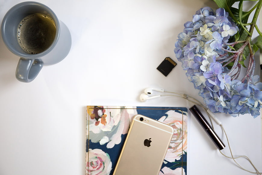 Flat lay of coffee, smartphone, and flowers on white desk