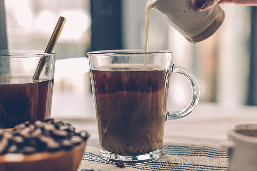 Pouring milk into a glass mug of black coffee