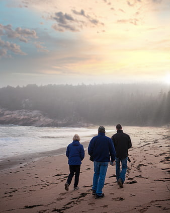 Three people walking on misty beach at sunset