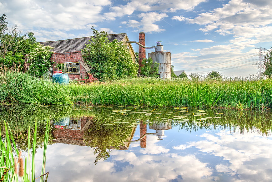 Abandoned brick factory with chimney reflected in pond