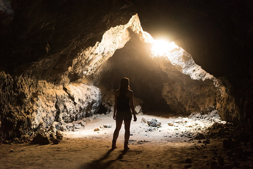 Woman standing in dark cave looking at light entrance