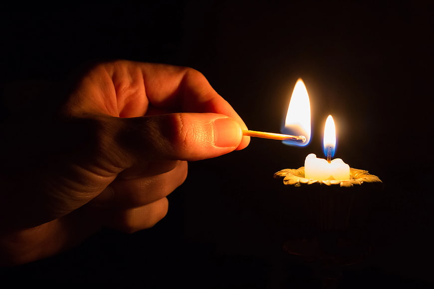 Hand Lighting Candle with Match in Dark Setting