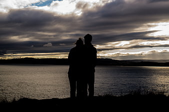 Silhouette of couple standing by lake at sunset
