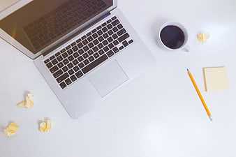 Top view of laptop, coffee, and stationery on white desk