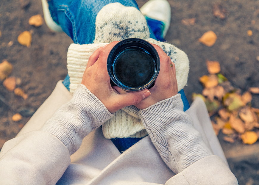 First-person view of hands holding a black coffee cup in autumn