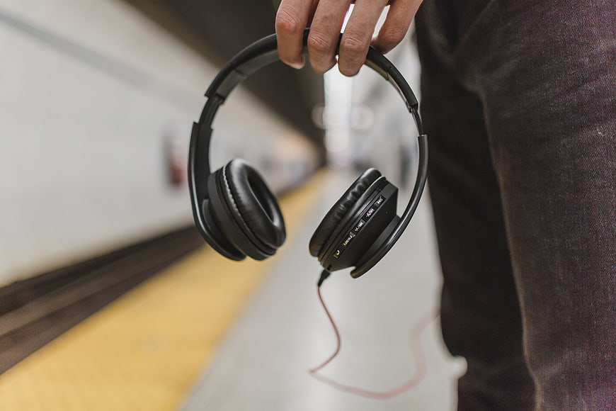 Hand holding black headphones on subway platform