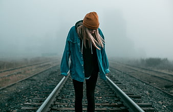 Sad woman in beanie standing on foggy train tracks