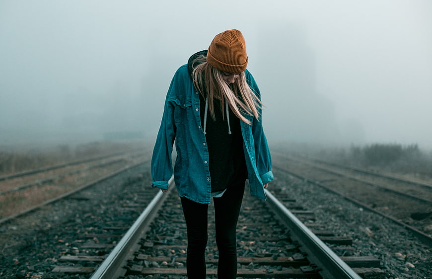 Sad woman in beanie standing on foggy train tracks