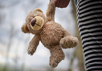 Child holding brown teddy bear outdoors