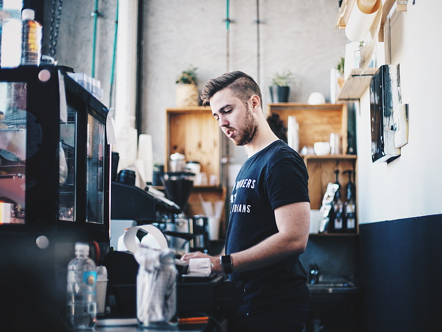 Young male barista working at coffee shop counter