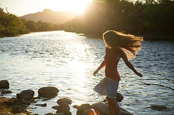 Woman with flowing hair walking on river rocks at sunset